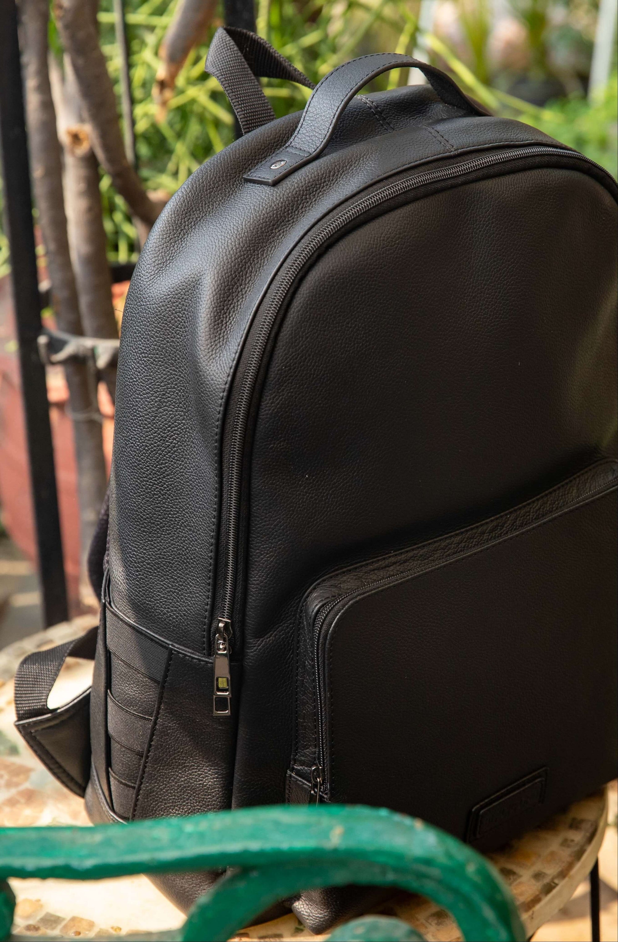 Black backpack on a green metal chair with a blurred natural background