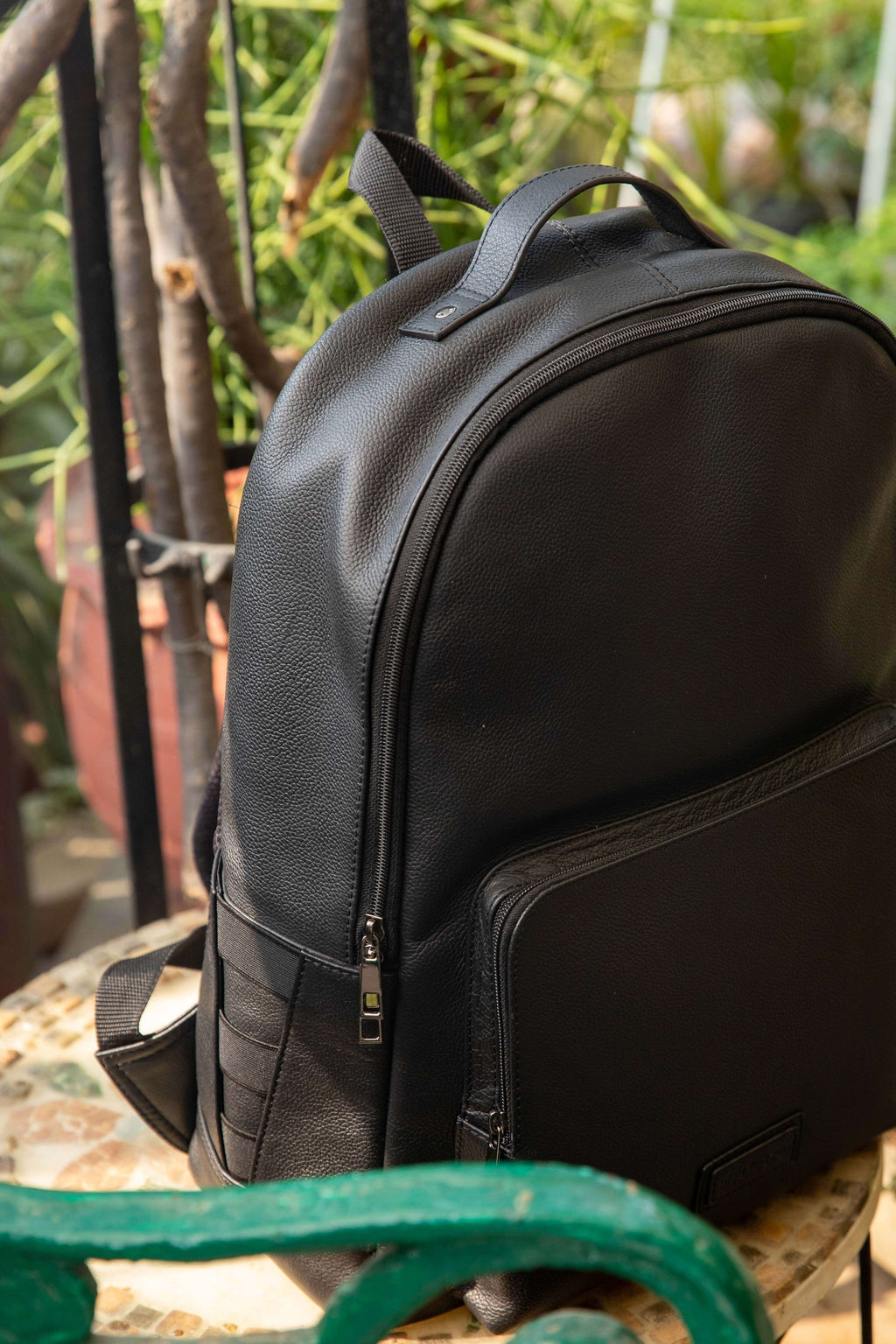 Black backpack on a green metal chair with a blurred natural background