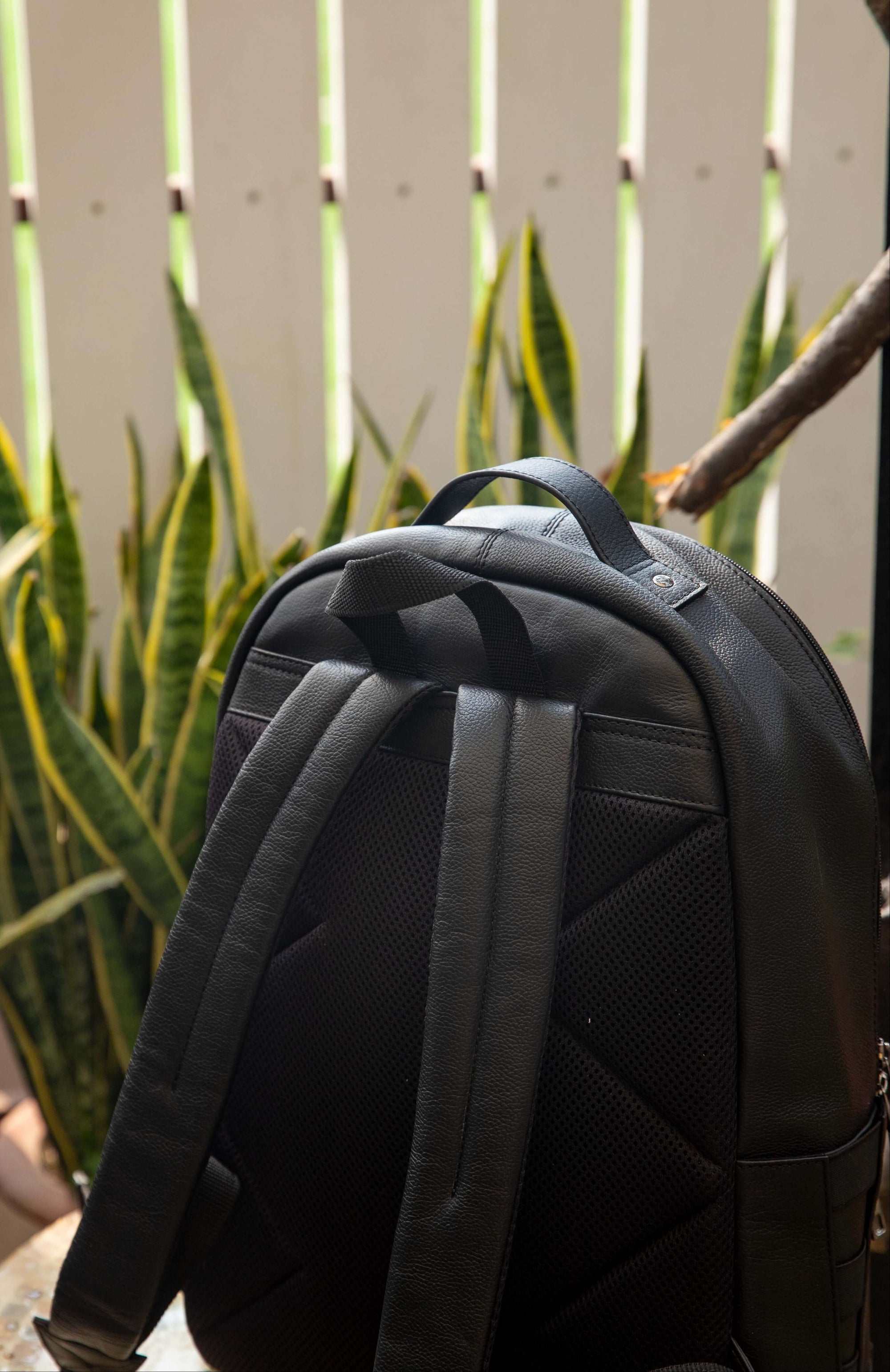 Black backpack against a white picket fence and green plants