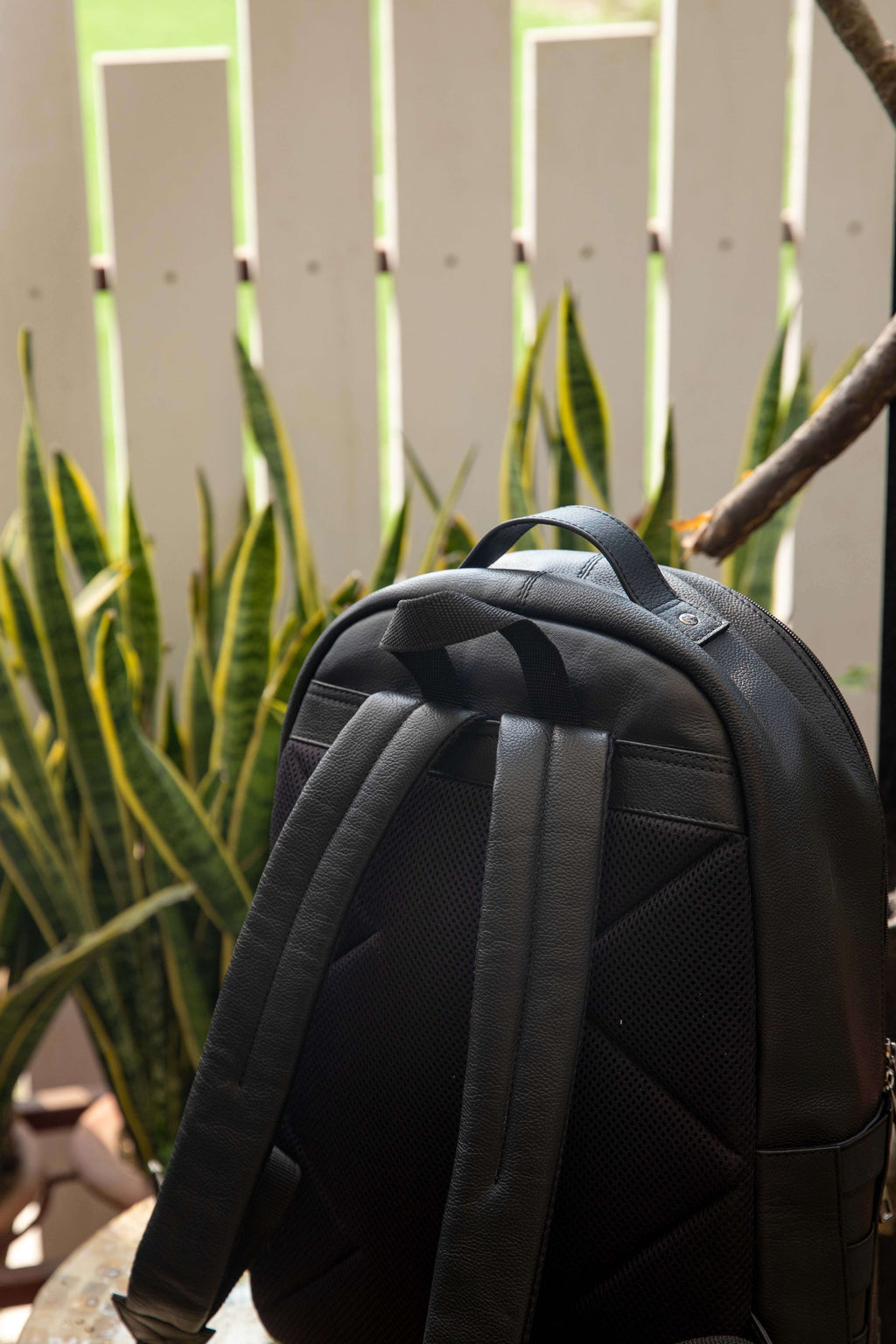 Black backpack against a white picket fence and green plants