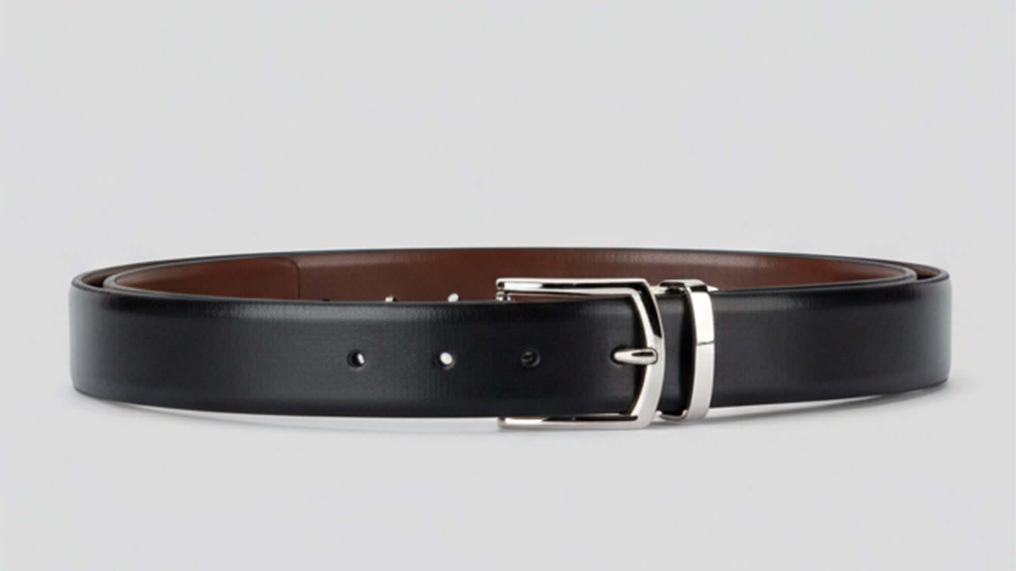 Black reversible leather belt with a silver buckle on a light gray background