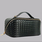 Black woven handbag with gold zippers on a gray background